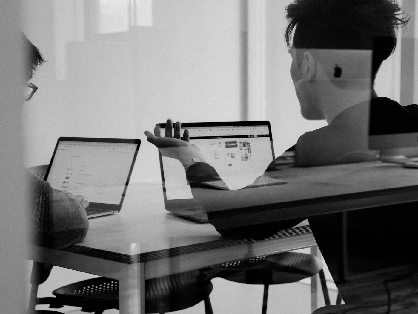 Two colleagues discussing work on laptops at a shared desk